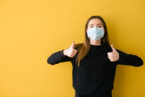 young girl in a protective mask on a yellow background shows a Like