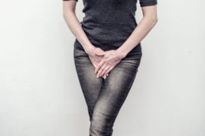 A photo of a woman standing with her legs crossed and her hands pressed into her pelvis with the urge to urinate.